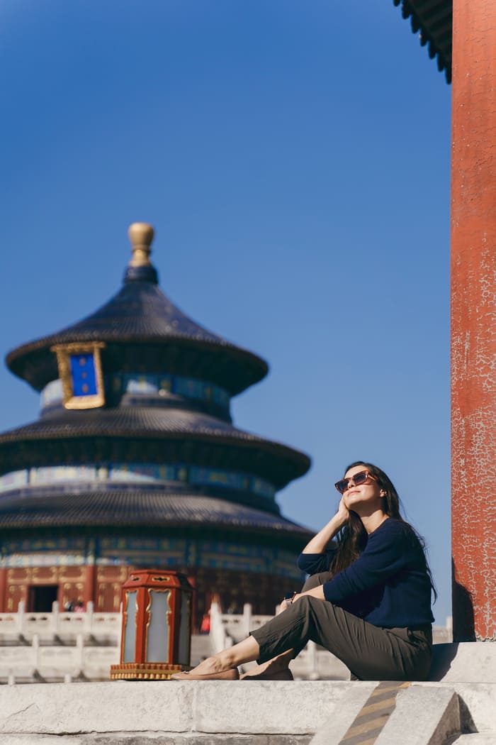 imagen de mujer mirando al sol de manera relajada sentada bajo la sombra de edificio chino y con fondo de edificio chino